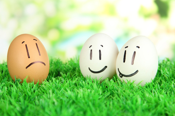 Eggs with funny faces on grass on bright background - 写真・画像