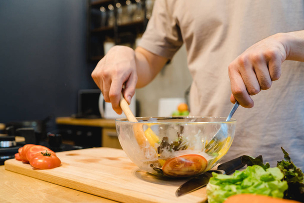 Boldog szép ázsiai ember saláta készithetik a konyhában. Fiatal ázsiai férfi egészséges ételt, míg otthon marad. Férfi életmód, otthon koncepció. - Fotó, kép