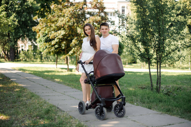 Happy parents and their little daughter in the babby carriage standing in the public park - Foto, Imagem
