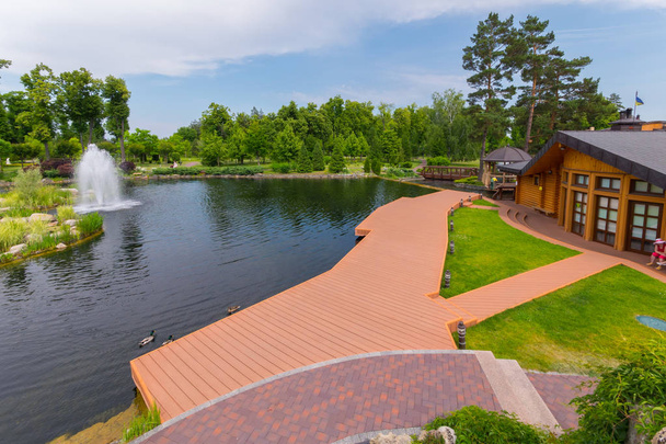 Una vista encantadora de la plataforma de madera de la orilla del estanque con los patos flotando a su lado y la fuente en el centro
 - Foto, imagen