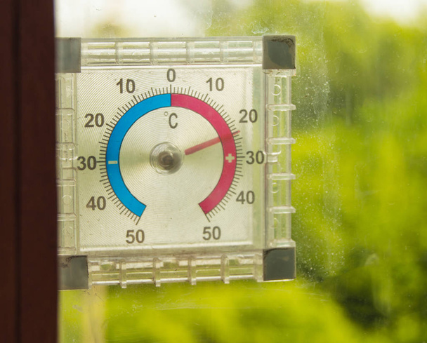 Termômetro de rua pendurado na janela e mostra a temperatura do ar no verão contra as árvores verdes
 - Foto, Imagem