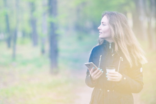 A lány egy séta reggel a park egy okostelefon, és kávé, könnyű alakformálás - Fotó, kép