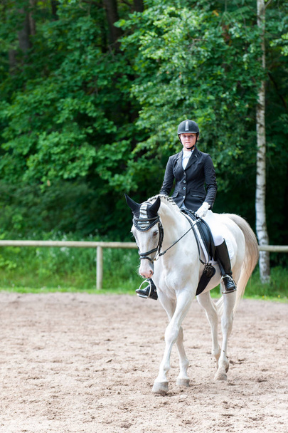 Adolescente chica ecuestre en uniforme de vestir a caballo en la arena en la competencia espectáculo. Vibrante imagen vertical multicolor al aire libre
. - Foto, imagen