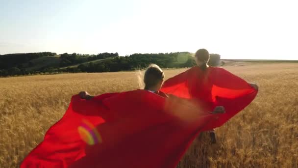 Las niñas juegan a los superhéroes corriendo por el campo con trigo en el resplandor de la luz del sol. Movimiento lento
 - Metraje, vídeo