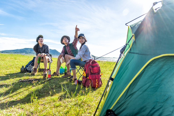 Group of hikers looking at attraction view point at meadow field with mountain and lake background. People and lifestyles concept. Hiking and Travel theme. Three people with backpack. Tent foreground - Photo, Image