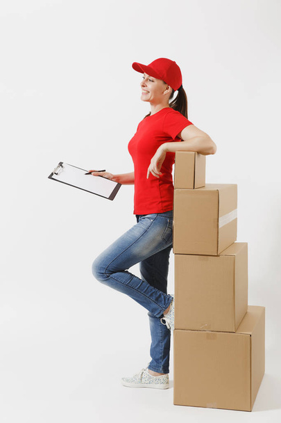 Full length of delivery woman in red cap, t-shirt isolated on white background. Female courier holding clipboard with papers document, blank empty sheet on empty cardboard boxes. Receiving package - Фото, зображення