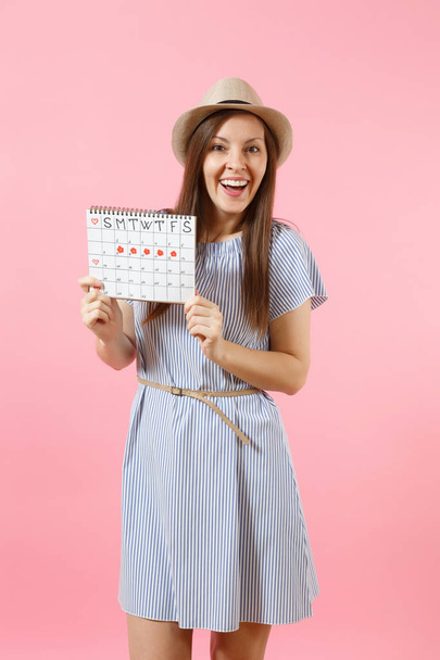 Portrait de jeune femme en robe bleue, chapeau tenant calendrier des périodes pour vérifier les jours de menstruation isolés sur fond rose vif. Médecine, santé, concept gynécologique. Espace de copie
 - Photo, image