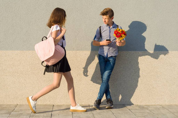 Outdoor portrait of teenagers, boy with bouquet of flowers and girl, gray wall background - Photo, Image