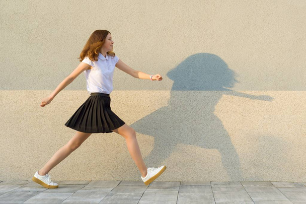 Young girl in the profile, walks along the gray wall, hurry, is late, takes big steps. Outdoor, copy space - Photo, image