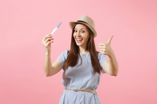 Excited happy woman in blue dress, hat hold in hand, looking at pregnancy test isolated on pink background. Medical healthcare gynecological, pregnancy fertility maternity people concept. Copy space - Photo, Image