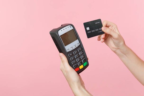Close up cropped photo of female holding in hands wireless modern bank payment terminal to process and acquire credit card payments, black card isolated on pink background. Copy space for advertising - Photo, Image
