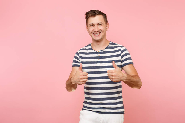 Portrait of excited smiling young man wearing striped t-shirt showing thumbs up gesture on copy space isolated on trending pink background. People sincere emotions lifestyle concept. Advertising area - Photo, Image
