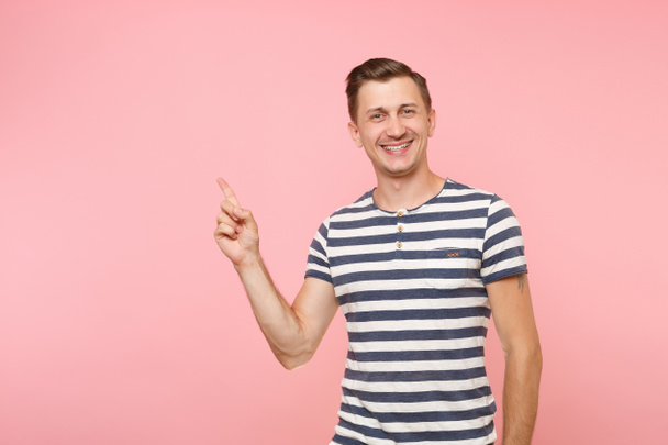 Portret enthousiast lachende jongeman met gestreepte t-shirt wijsvinger van index opzij op kopie ruimte geïsoleerd op trending roze achtergrond. Mensen oprechte emoties levensstijl concept. Gebied van de reclame. - Foto, afbeelding