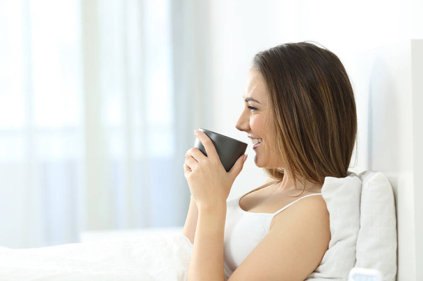Side view portrait of a girl drinking coffee at breakfast in the morning on the bed at home - Foto, imagen