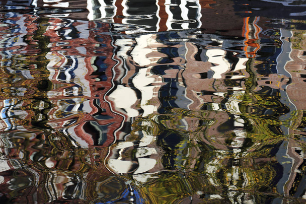 Искаженное зеркальное отражение исторических зданий в воде канала в Амстердаме, Голландия
 - Фото, изображение