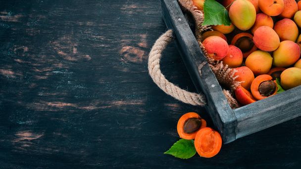 Apricots in a wooden box. Fresh fruits. On a black wooden background. Top view. Free space for your text. - Foto, immagini