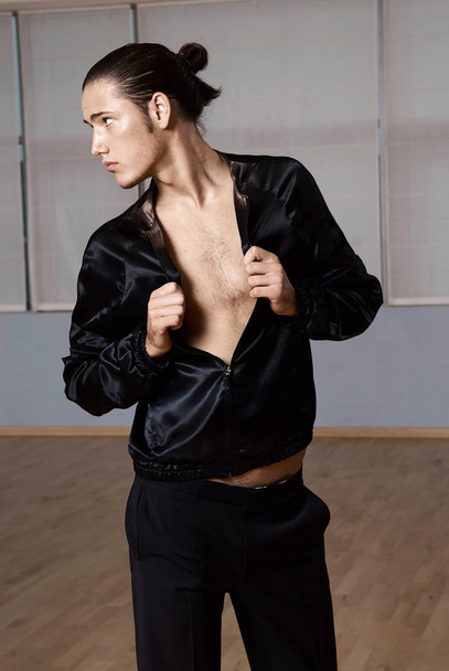 Mann in eleganter Suite posiert im Fitnessstudio. High Fashion junger sexy Mann in schwarzen Shorts und schwarzer Jacke. - Foto, Bild