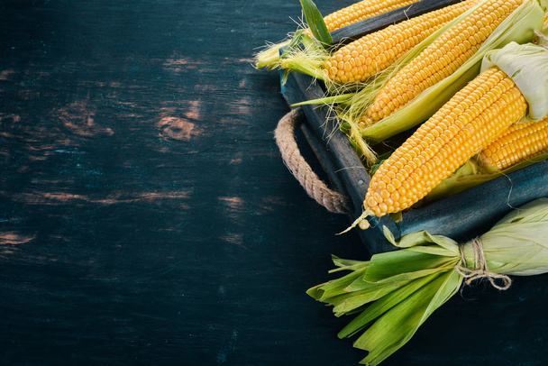 corn in a wooden box. Fresh vegetables. On a black wooden background. Top view. Copy space. - Foto, afbeelding