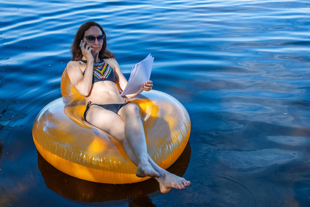 Business woman working on vacation, remote work. Woman talking on mobile phone while sitting in an inflatable ring - Valokuva, kuva