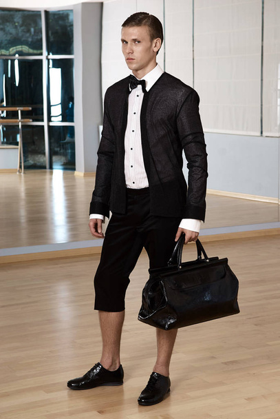 Male fashion, beauty concept. Elegant young fashion man holds in his hand a black bag and looking to away from the camera. Classic style. Studio shot - Foto, afbeelding