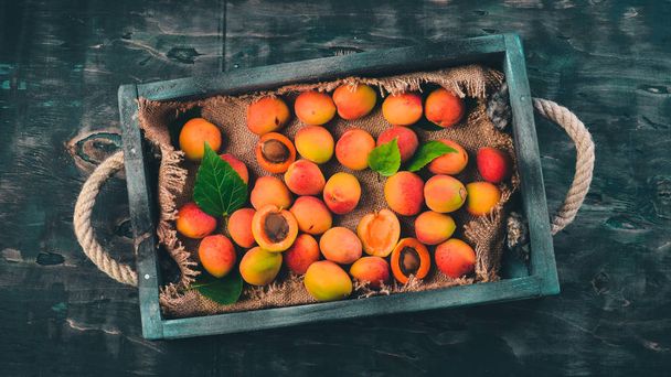 Apricots in a wooden box. Fresh fruits. On a black wooden background. Top view. Free space for your text. - Valokuva, kuva