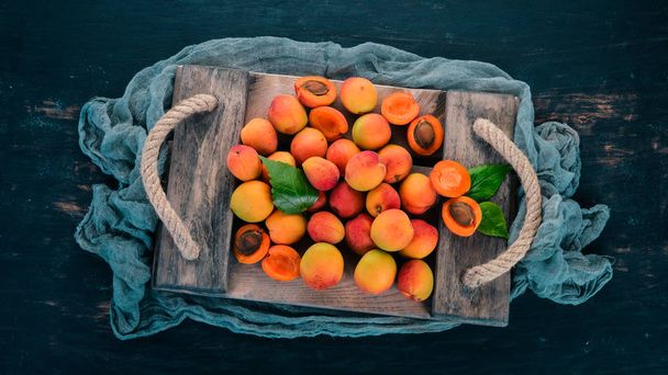 Apricots in a wooden box. Fresh fruits. On a black wooden background. Top view. Free space for your text. - Фото, зображення