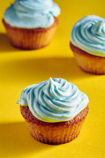 Unusual cupcakes with a beautiful blue cream. Cakes with perfect caps made from protein cream. Whipped cream with blue food color. Treat for children on a yellow-blue background. - Photo, Image
