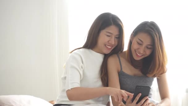 Yatak sarılmak üzerinde oturan ve evde telefon birlikte yatak odası kullanarak güzel genç Asyalı kadınlar Lgbt lezbiyen mutlu çift. LGBT lezbiyen birlikte kapalı kavramı çift. Evde güzel vakit. - Video, Çekim