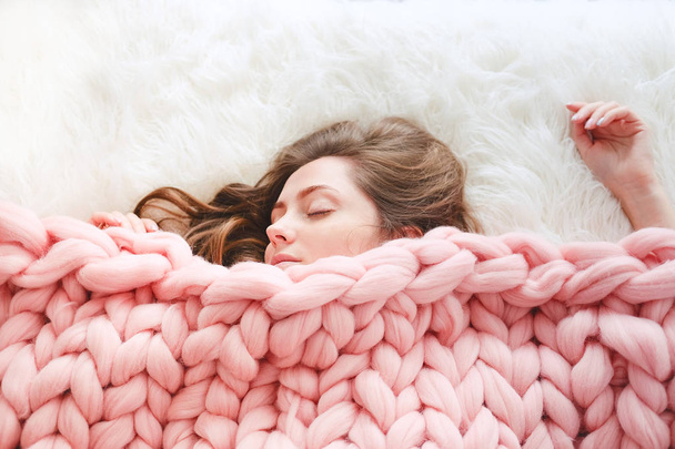 Mujer joven con cabello castaño largo durmiendo bajo una manta de color melocotón de punto cálido
 - Foto, Imagen