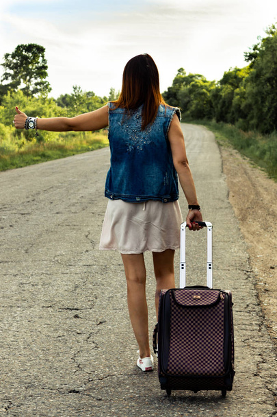 Chica con una maleta para el coche en la carretera
 - Foto, Imagen