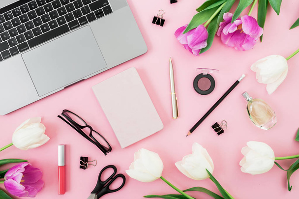 Draufsicht auf Laptop, umgeben von frischen Tulpen und Kosmetikprodukten auf rosa Hintergrund - Foto, Bild