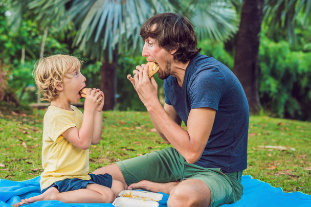 Portret młodego ojca i syna, ciesząc się hamburger w parku i uśmiechając się. - Zdjęcie, obraz