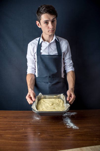 Youngman chef in uniform black apron prepares the dough for baking the cake. The concept of men cook desserts - Fotoğraf, Görsel