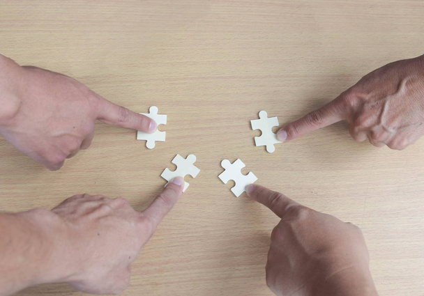 Groupe de gens d'affaires assemblant puzzle voulant mettre des morceaux de puzzle ensemble sur la table en bois backgragara pour aider à soutenir, concept de travail d'équipe
 - Photo, image