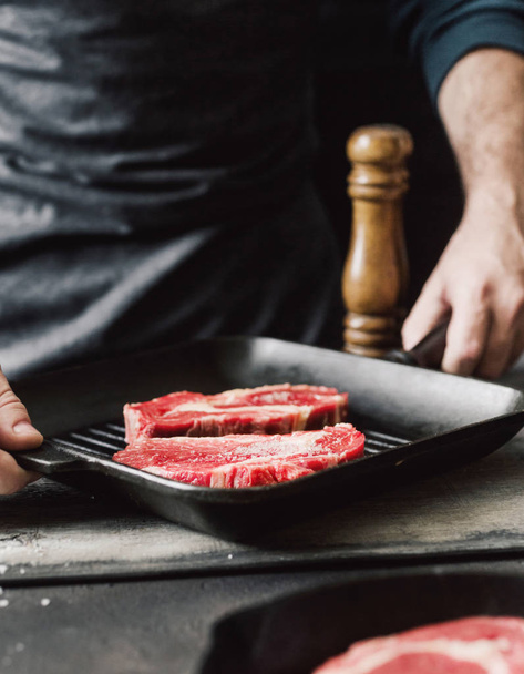 Male hands holding grill pan with beef raw steaks. Grilling steak cooking - Foto, immagini