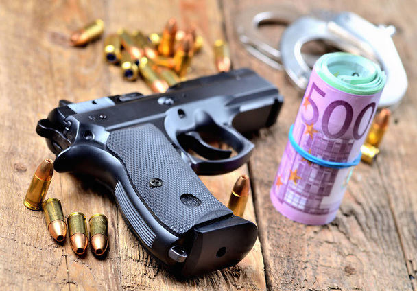 Пистолет калибра 9 мм, пули, наручники и рулон банкнот евро
 - Фото, изображение