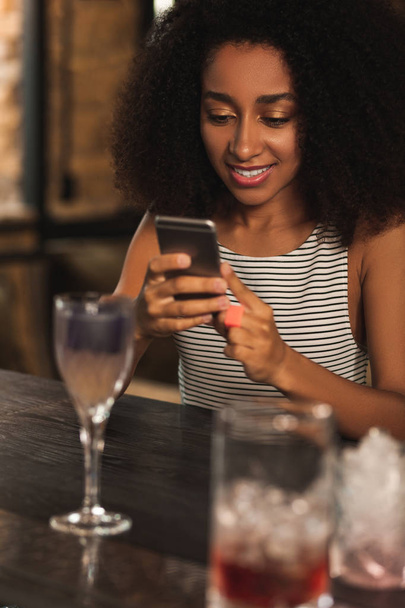 Beautiful curly woman texting while having cocktail in bar - Foto, Imagem