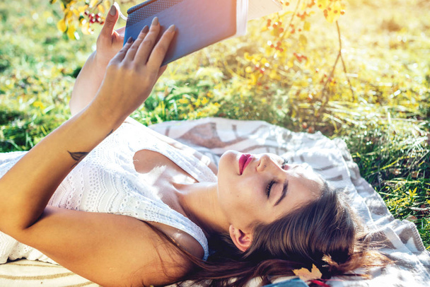 Atrakcyjna kobieta czytając ciekawą książkę leżąc w parku na zielony trawnik na słoneczny jesienny dzień. Koncepcja kształcenia studentów - Zdjęcie, obraz