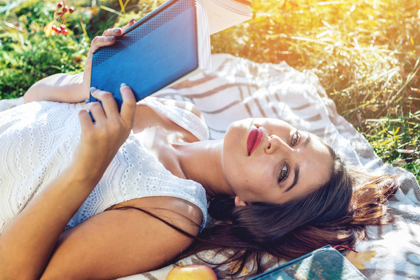 Belle femme lisant un livre intéressant couché dans le parc sur une pelouse verte un jour d'automne ensoleillé. Le concept de l'éducation des étudiants
 - Photo, image