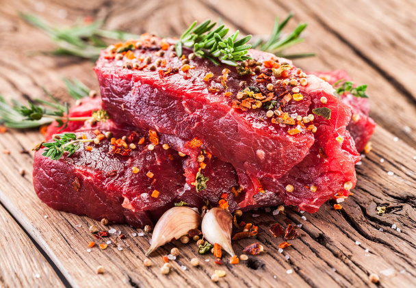 Beef steaks with seasonings on the wooden table. - Foto, afbeelding