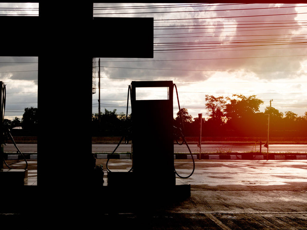 Silhueta close-up bomba de gasolina bico de enchimento. Posto de gasolina à noite na estrada do pôr do sol depois de chover fundo
. - Foto, Imagem
