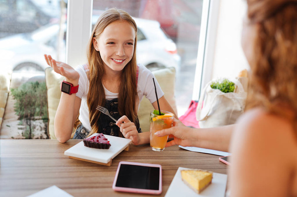 Smiling girl eating dessert and drinking cocktail with mother - Photo, image