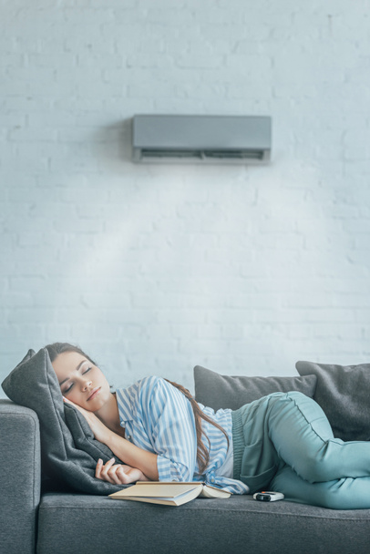 woman sleeping on couch with book and air conditioner blowing on her - Foto, Bild