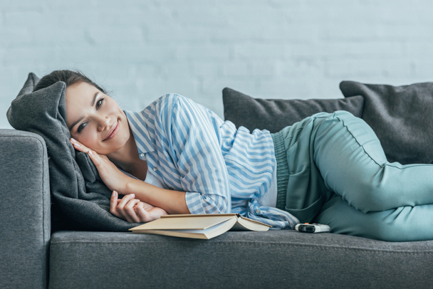 smiling woman relaxing on sofa with book  - Photo, Image