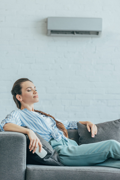 nő nyugszik kanapé van légkondicionáló berendezés a falon, nyári hő koncepció - Fotó, kép