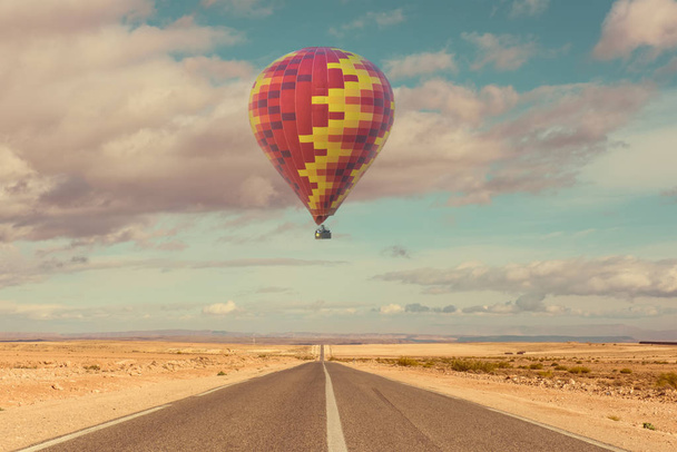 Hot air balloon over desert and road - 写真・画像