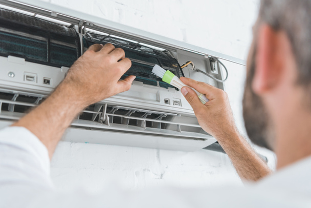 selective focus of repairman cleaning air conditioner with brush - Valokuva, kuva