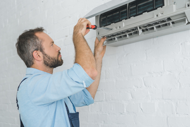 reparateur vaststelling van airconditioner met schroevendraaier op zomerhitte - Foto, afbeelding