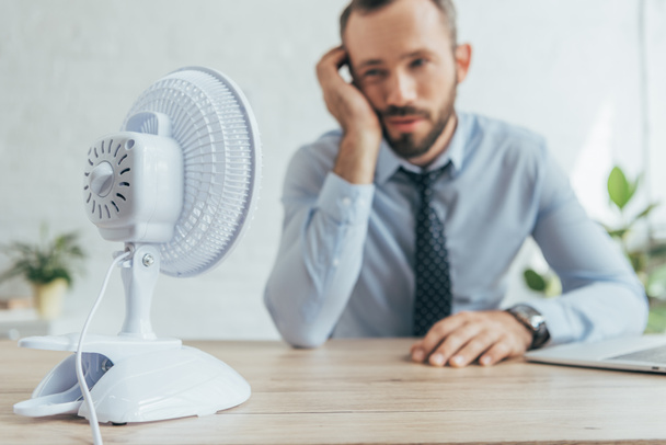 Selektivní fokus podnikatel v úřadu s bílým elektrický ventilátor - Fotografie, Obrázek