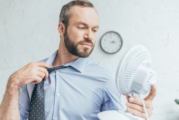businessman removing tie and blowing on himself with white electric fan   - Foto, Imagem